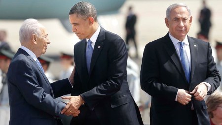 Barack Obama amerikai elnök kezet fog Simon Peresz izraeli elnökkel a tel-avivi Ben Gurion repülőtéren 2013. március 20-án, a háttérben Benjamin Netanjahu izraeli miniszterelnök